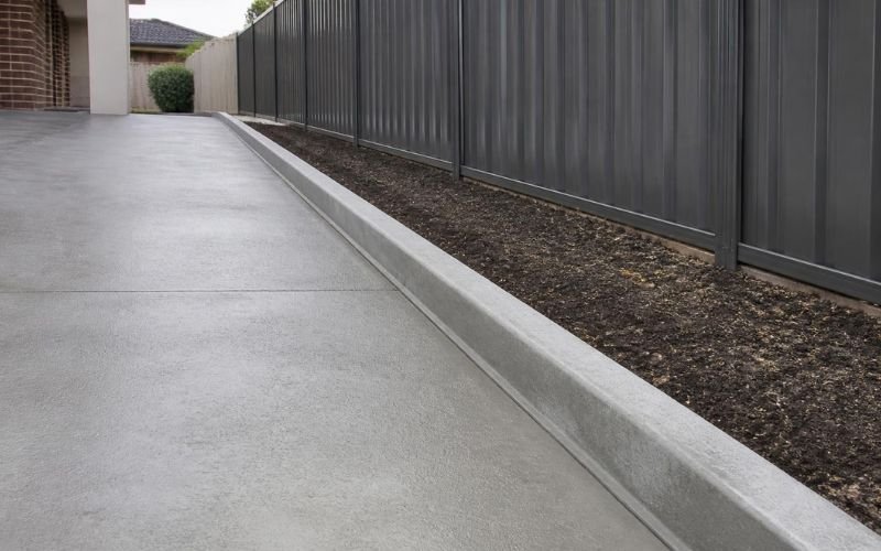 concrete edging stopping paving runoff at boundary fence